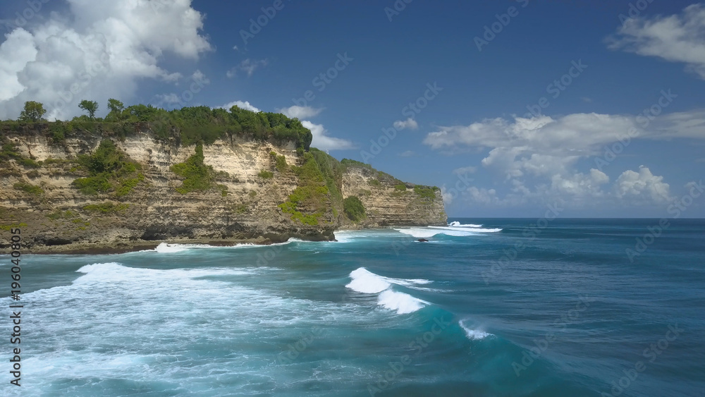 Panoramic view of the endless blue ocean waves crashing into majestic cliff.
