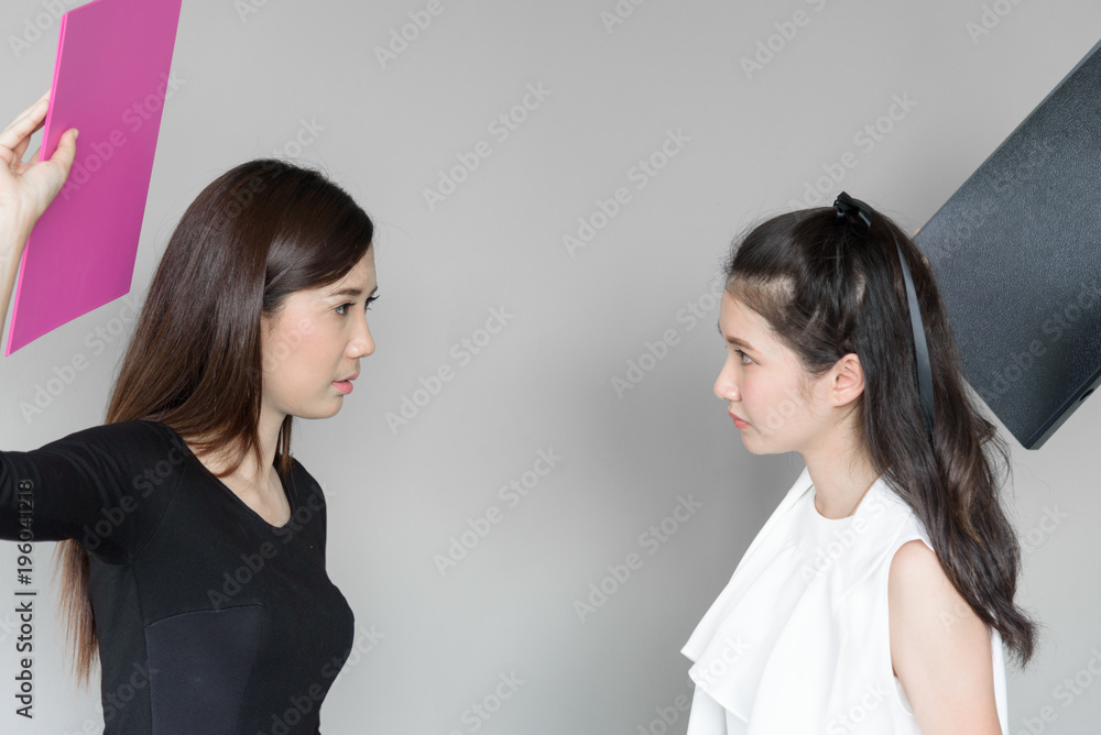 Businesswomen workmate has use a pink and black folder for hitting and fighting with angry and upset in the office isolated and grey background. Businesswomen workmate has use a pink and black folder for hitting and fighting with angry and upset in the office isolated and grey background.