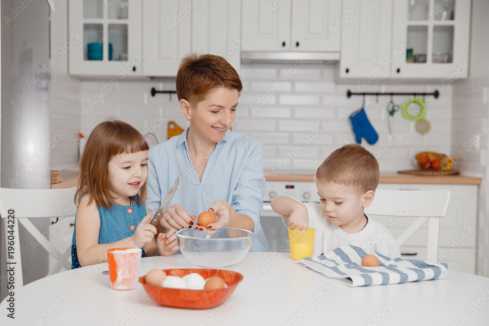 Children together with their mother are preparing cupcake for their father, Caucasian family in kitchen at white dining table. Masterclass of cake making. Children together with their mother are preparing cupcake for their father, Caucasian family in kitchen at white dining table. Masterclass of cake making.