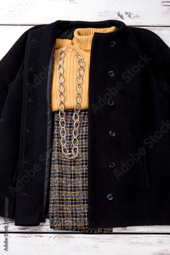 Folded winter outfit with chain necklace. White wooden desks surface background.