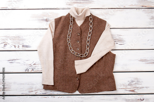 Brown sleeveless jacket with necklace. Bright beige white wooden desks surface background.