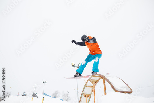Photo of young sportive man skiing on snowboard with springboard against snowy sky in winter