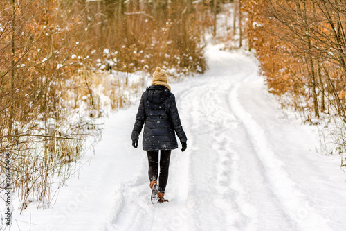 Woman on snow road in winter, girl in black coat, back view in the forest photo