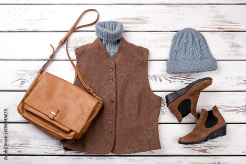 Brown female winter look with handbag. White wooden background, flat lay top view.