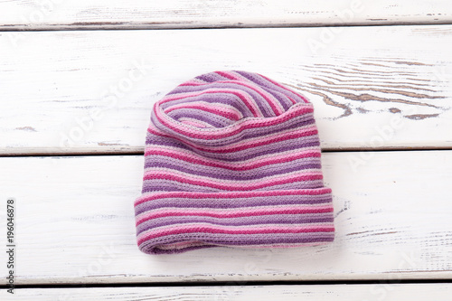 Pink striped woolen hat. Flat lay, top view. White wooden desks surface background. photo