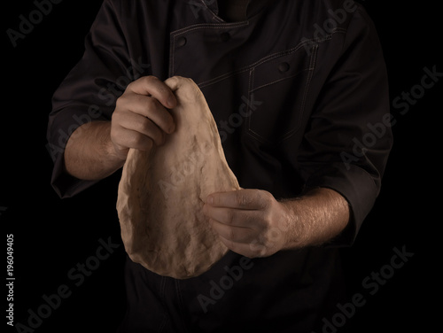 Hands of the Baker knead layer of dough, isolated on black