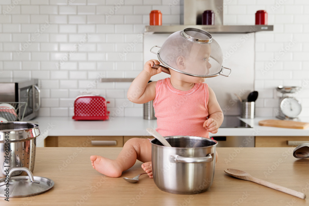 Baby sitting on kitchen counter with strainer on his head Stock Photo