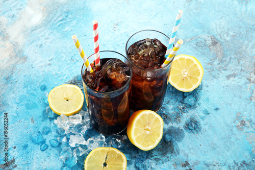 Softdrink with ice cubes, lemon and straw in glass.