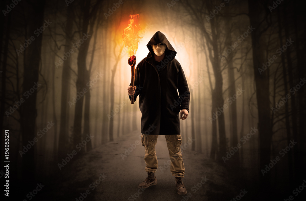 Man coming from dark forest with burning flambeau in his hand concept