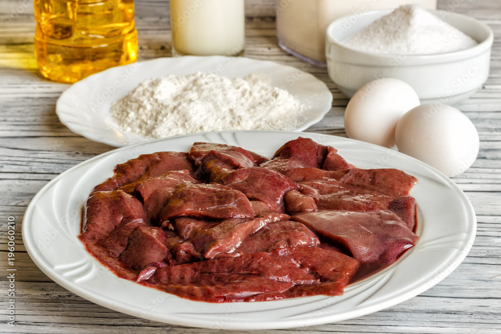 Raw liver on a white plate on a wooden background. A set of products for cooking fried liver egg oil salt flour. Food ingredient. Selective focus.