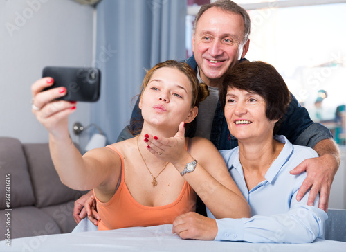 Marrieds with their adult daughter are takinf selfie together on sofa photo