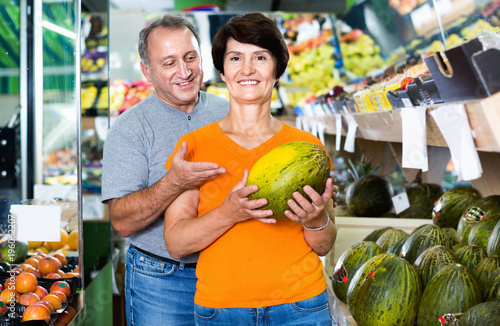Adult male and female are choosing green melons in the store.