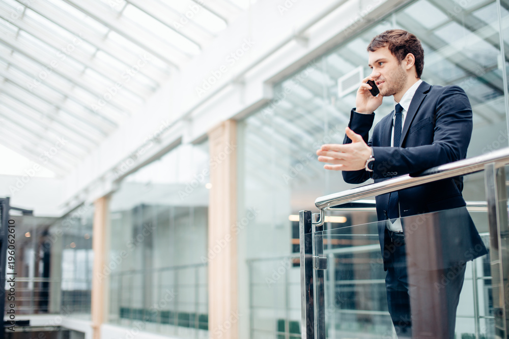 Portrait of cheerful men office worker talking on mobile phone while standing in modern office Portrait of cheerful men office worker talking on mobile phone while standing in modern office