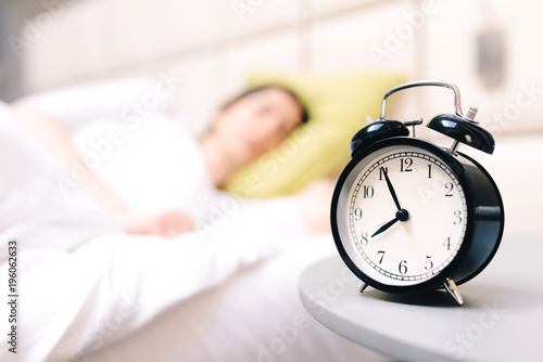 Young sleeping woman and alarm clock in bedroom at home - very shallow depth of field