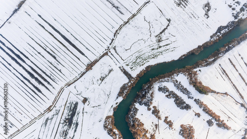 Aerial view riverbend passing snow covered fields.