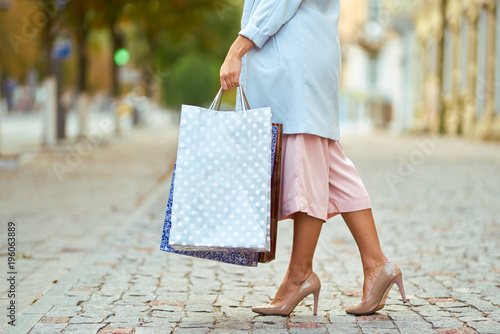 Closeup of woman holding shopping bags on the street with copy space. Happy woman with shopping bags enjoying in shopping. Consumerism, shopping lifestyle concept.
