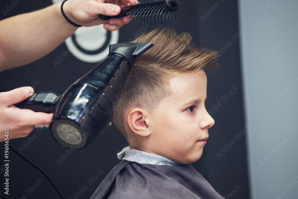 Hairdresser making a hairstyle to a boy in barbershop.