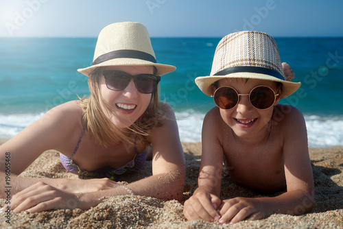 Mom and son in sunglasses are having a rest on the beach against the sea.
