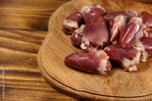 Raw chicken hearts on cutting board on wooden table
