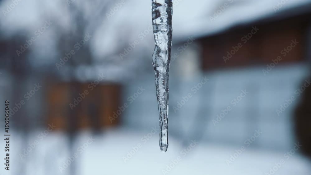 Long shiny icicle hanging from rooftop in suburbs. Long shiny icicle hanging from rooftop in suburbs.