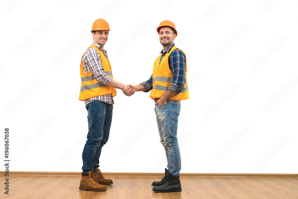 The two happy engineers handshake on the white wall background The two happy engineers handshake on the white wall background