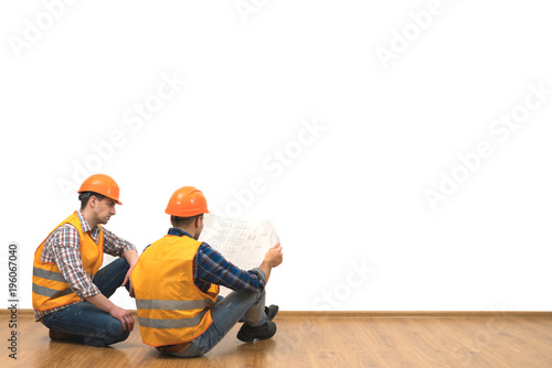 The two engineers with a paper sit on the floor on the white wall background