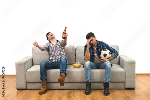 Fotografia The two men with a beer and chips watch a football on the sofa