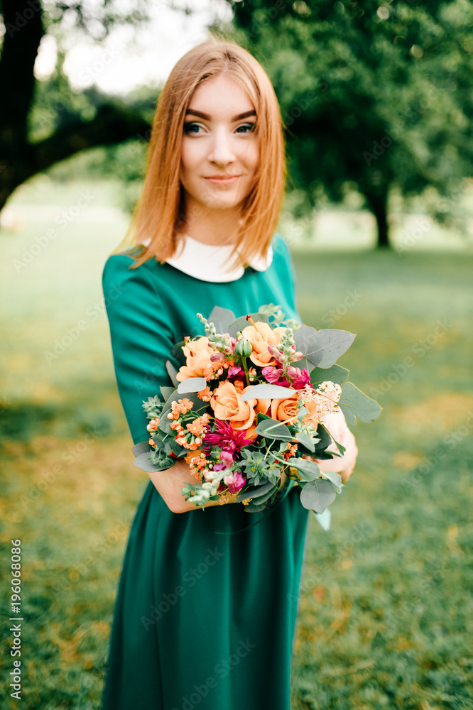 Young happy red haired girl with bouquet of summer flowers enjoying inner peace in green dress at nature. Little child playing in wonderland park. Pretty woman portrait outdoor. Lovely smiling face. Young happy red haired girl with bouquet of summer flowers enjoying inner peace in green dress at nature. Little child playing in wonderland park. Pretty woman portrait outdoor. Lovely smiling face.