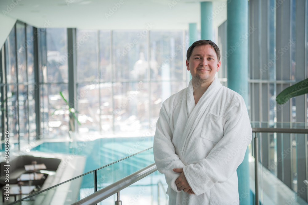 Fototapeta premium Adult man in a bathrobe standing in the spa in front of a pool
