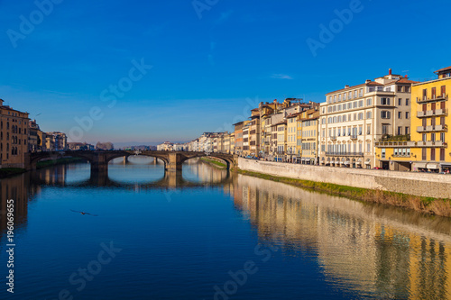 Cityscape view on Arno river with famous Holy Trinity bridge in Florence. Reflections on water. Old colorful houses on the side. Tuscany, Italy