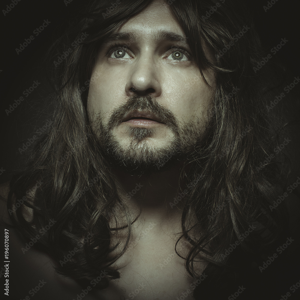 faith concept, man with intense gaze and long hair looking towards the light in prayer pose