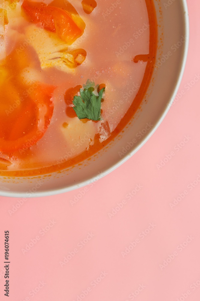 Hot vegetable soup with chicken meat in a bowl. a leaf of greenery. on a pink background. The concept of a healthy food and diet. Closeup. Hot vegetable soup with chicken meat in a bowl. a leaf of greenery. on a pink background. The concept of a healthy food and diet. Closeup.