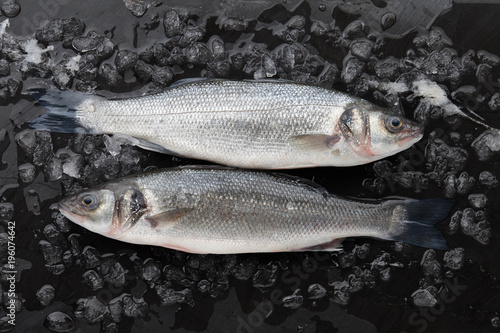 Two red seabass fish on ice on black stone background, top view
