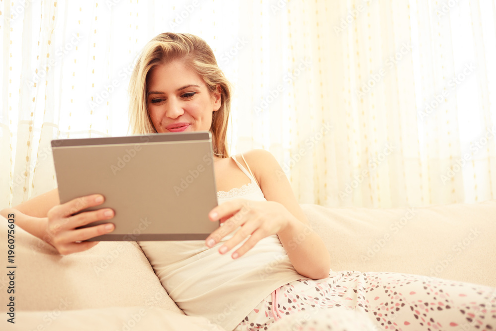 Beautiful happy young girl lying in pajamas and smiling while using a tablet in bed Beautiful happy young girl lying in pajamas and smiling while using a tablet in bed