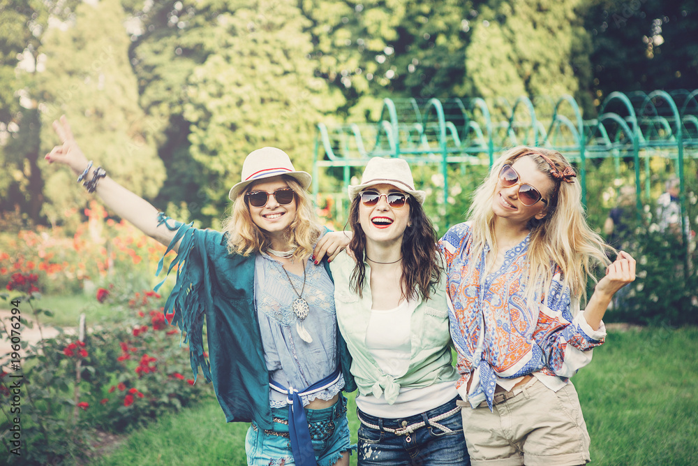 Fototapeta premium Happy friends in the park on a sunny day . Summer lifestyle portrait of three hipster women enjoy nice day, wearing bright sunglasses. Best friends girls having fun, joy. Lifestyle