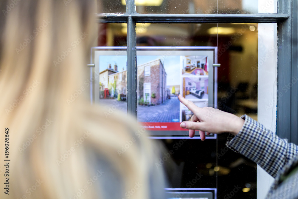 Couple looking at a property advert in the window of an estate agents or real estate shop window in England in the United Kingdom - obrazy, fototapety, plakaty 