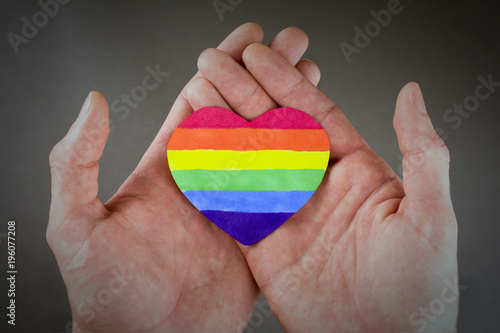 LGBT day concept  heart LGBT rainbow flag in the hands. Gray background