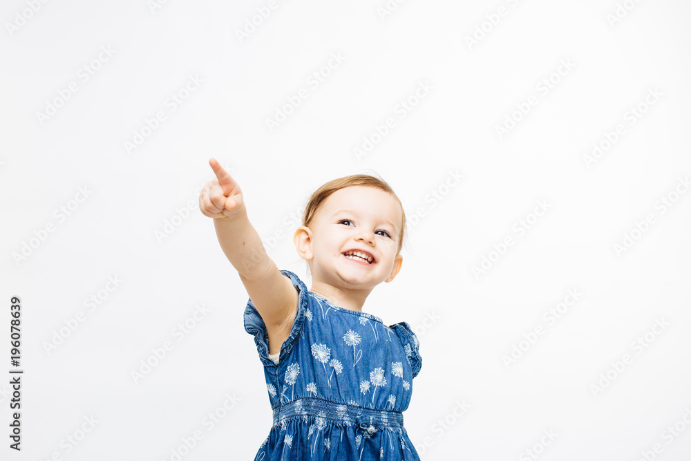 A very excited and happy toddler girl pointing up with one finger, isolated on white studio background A very excited and happy toddler girl pointing up with one finger, isolated on white studio background