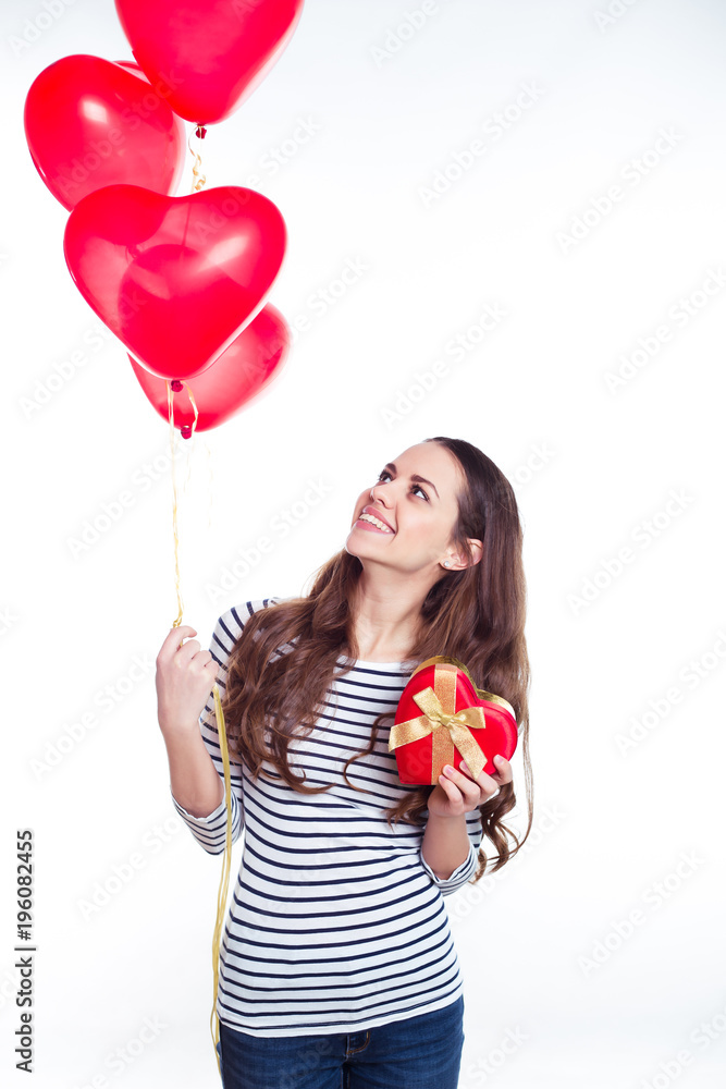 Gifts for the beloved. Beautiful smiling young woman in casual clothing with helium balloons and a gift in the form of heart in her hands. Valentine's Day. Birthday. Gifts for the beloved. Beautiful smiling young woman in casual clothing with helium balloons and a gift in the form of heart in her hands. Valentine's Day. Birthday.