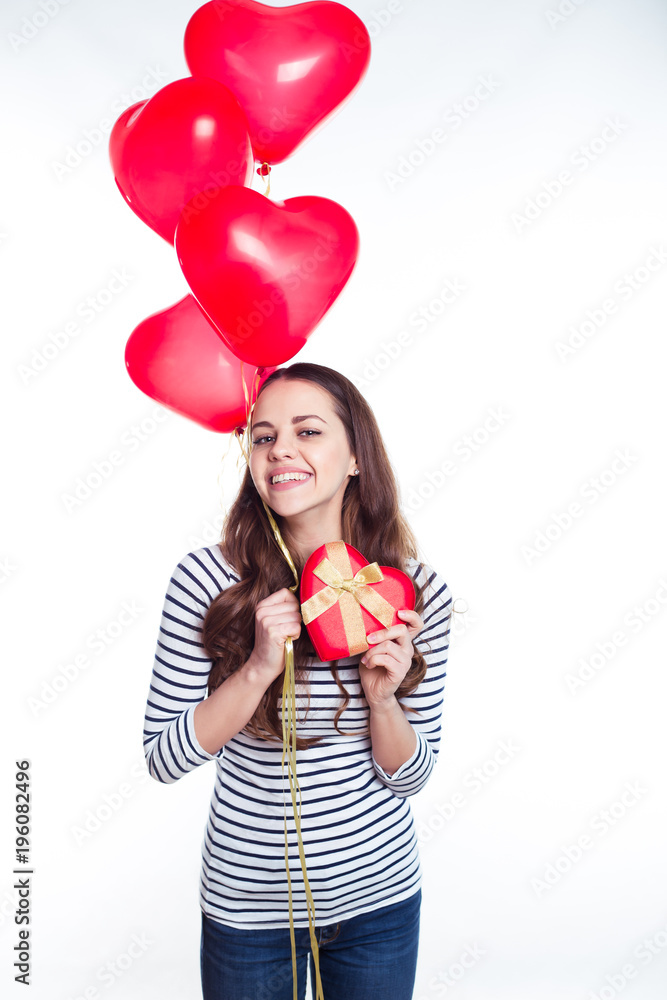 Gifts for the beloved. Beautiful smiling young woman in casual clothing with helium balloons and a gift in the form of heart in her hands. Valentine's Day. Birthday. Gifts for the beloved. Beautiful smiling young woman in casual clothing with helium balloons and a gift in the form of heart in her hands. Valentine's Day. Birthday.