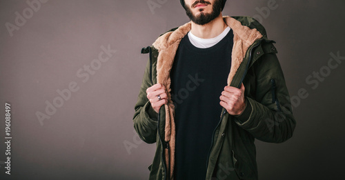 Young bearded man in denim jacket with shearling liner shows his chest wearing black unlabeled henley shirt longsleeve  isolated on grey wall in studio