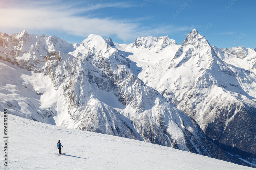 Alone skier descends the mountainside against the background of the mountains of the Caucasus, Dombai on a winter sunny day