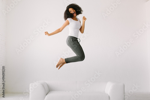 An African American young woman jumping on white bed