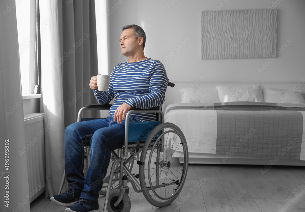 Mature man in wheelchair drinking coffee near window indoors Mature man in wheelchair drinking coffee near window indoors