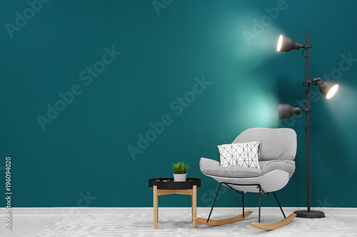 Trendy living room interior with comfortable armchair against shaded spruce wall