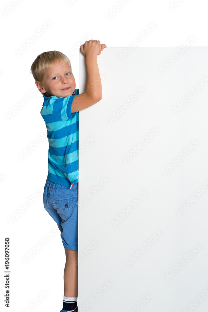 A little boy is looking from behind an empty banner.