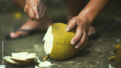 Close up shot of a Vietnamese man using a machete to cut open the top of a coconut as coconut water spills out