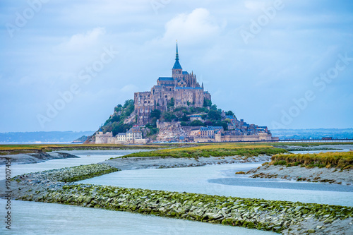 Beautiful panoramic view of famous Le Mont Saint-Michel tidal island with deep blue water in grey evening light at sunset in autumn, Normandy, northern France