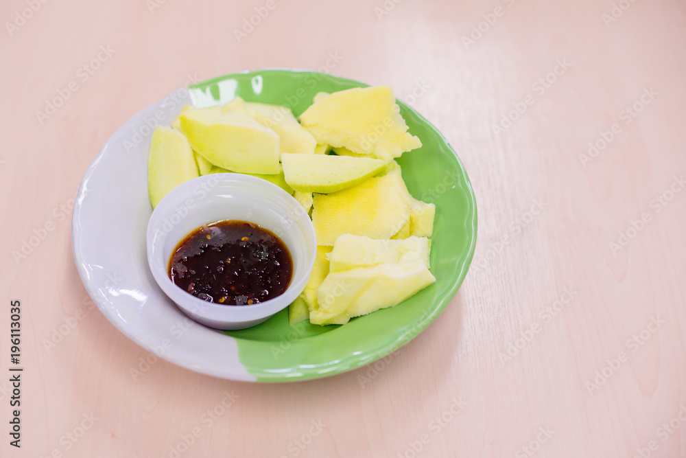 Sliced mango and sweet fish sauce in dish on wooden table Sliced mango and sweet fish sauce in dish on wooden table