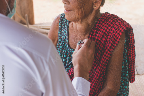 Male Doctor listening heart beat and breathing of Elderly Woman with Stethoscope with First Aid Medical Box.Community Health and Development Hospital In Remote Areas Development Fund Concept.